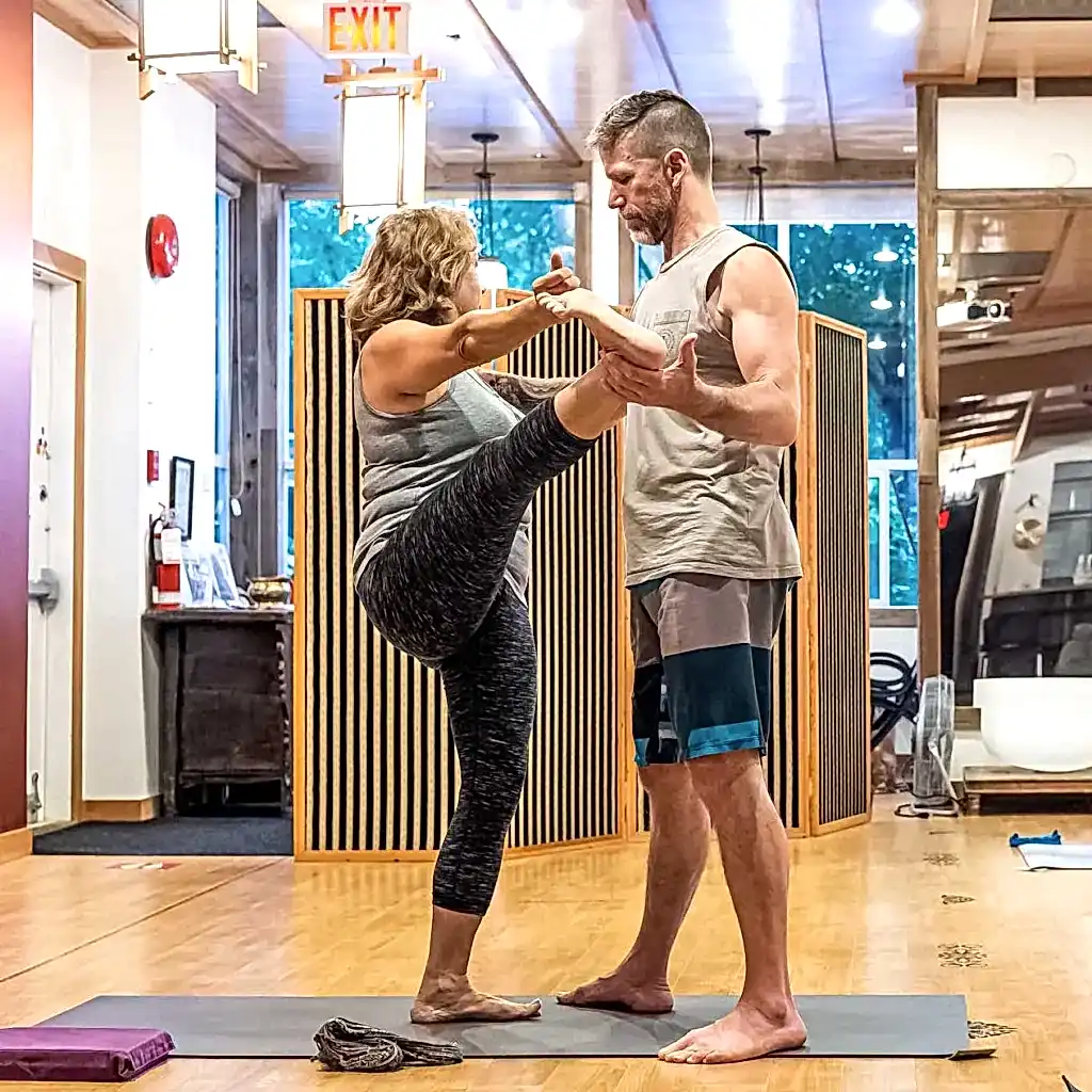 first light yoga, the method, geoff assisting a student with a standing posture in class